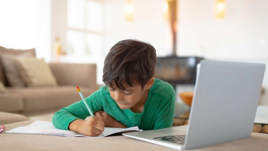 Front view of African american boy using laptop while drawing a sketch on book at home