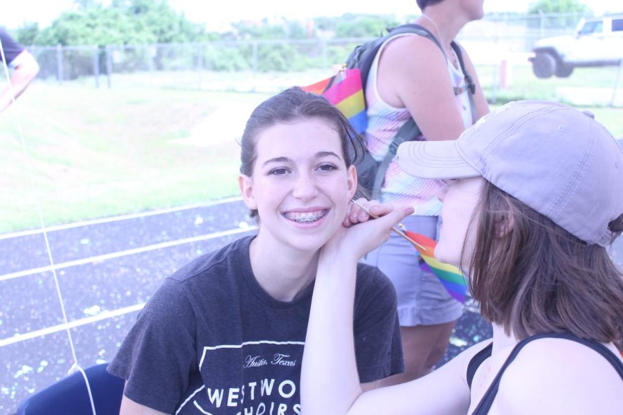 A member of Westwood High Schools Drama Club doing face paint on a student.